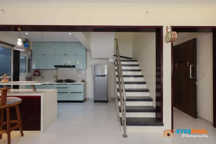 Open mint-green kitchen beneath a staircase, with a breakfast counter alongside