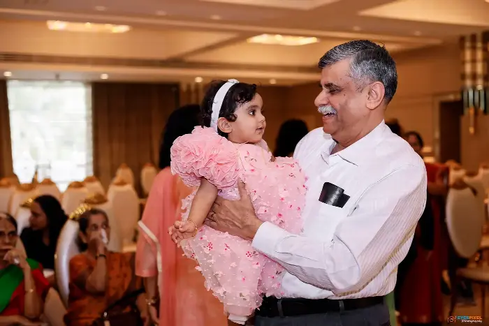 Grandfather holding his granddaughter in a pink dress at her first birthday party
