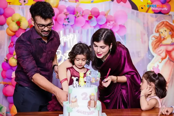 Family cutting a two-tier second birthday cake together at a themed party