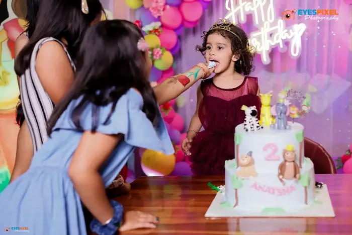 Girl being fed a spoonful of her second birthday cake by an older sister