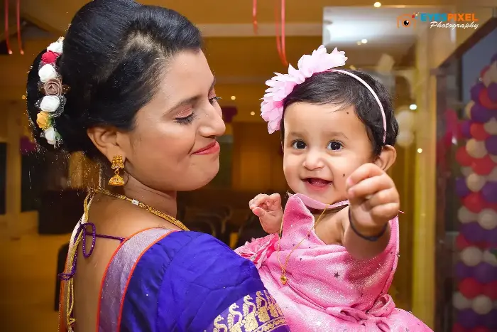 Mother holding her smiling baby daughter in pink at a birthday celebration