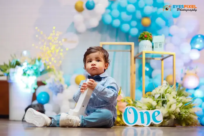First birthday boy sitting on the floor in front of a blue balloon wall holding a decoration
