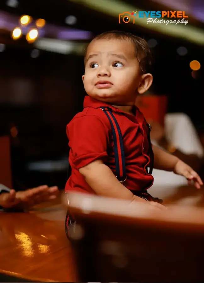 One-year-old in a red shirt and braces looking over his shoulder in a restaurant