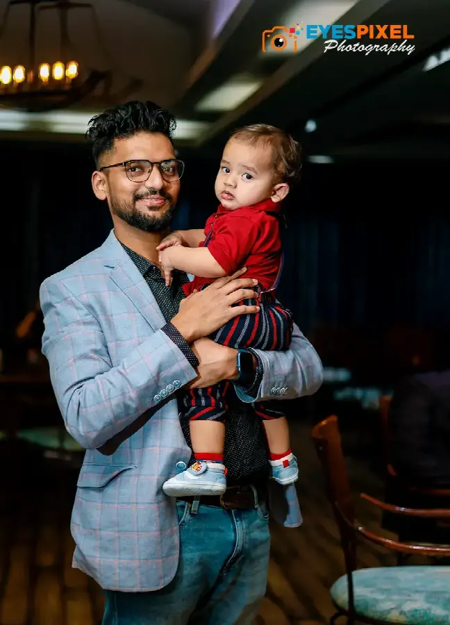 Father in a checked blazer holding his son in a red shirt at a restaurant celebration