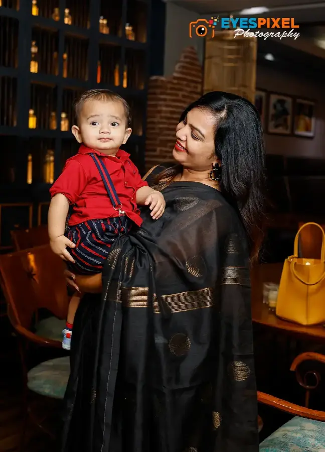 Mother in a black saree holding her son in a red shirt and braces at a restaurant