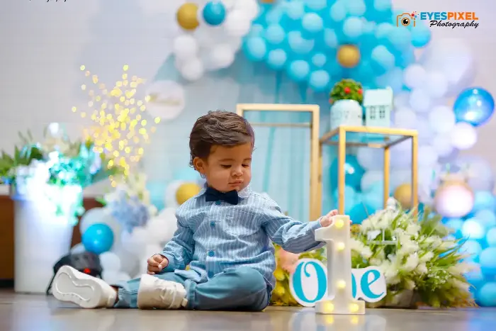 First birthday boy reaching towards an illuminated number one at a blue and white party setup