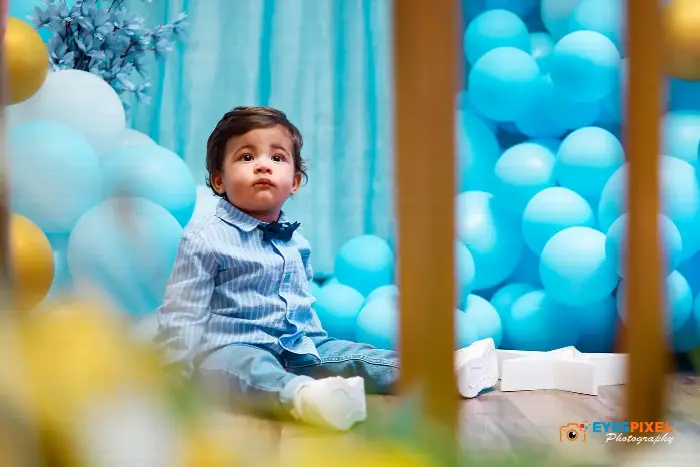 First birthday boy framed between decor, blue balloons filling the background