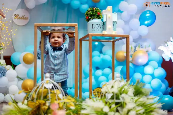 Toddler standing and holding a display frame at a blue balloon birthday backdrop with a name plaque