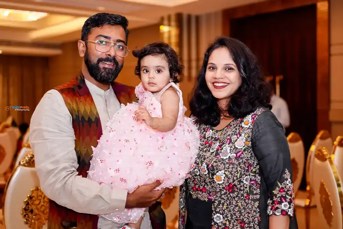 Parents holding their one-year-old in a pink dress at her birthday celebration in a banquet hall