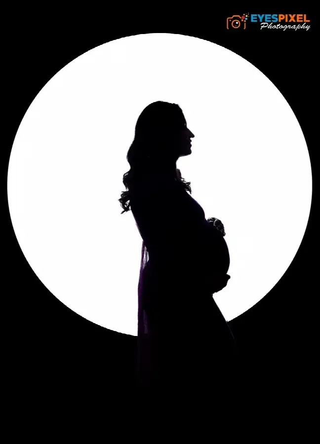 Silhouette of an expectant mother in profile against a bright circular light, maternity studio portrait