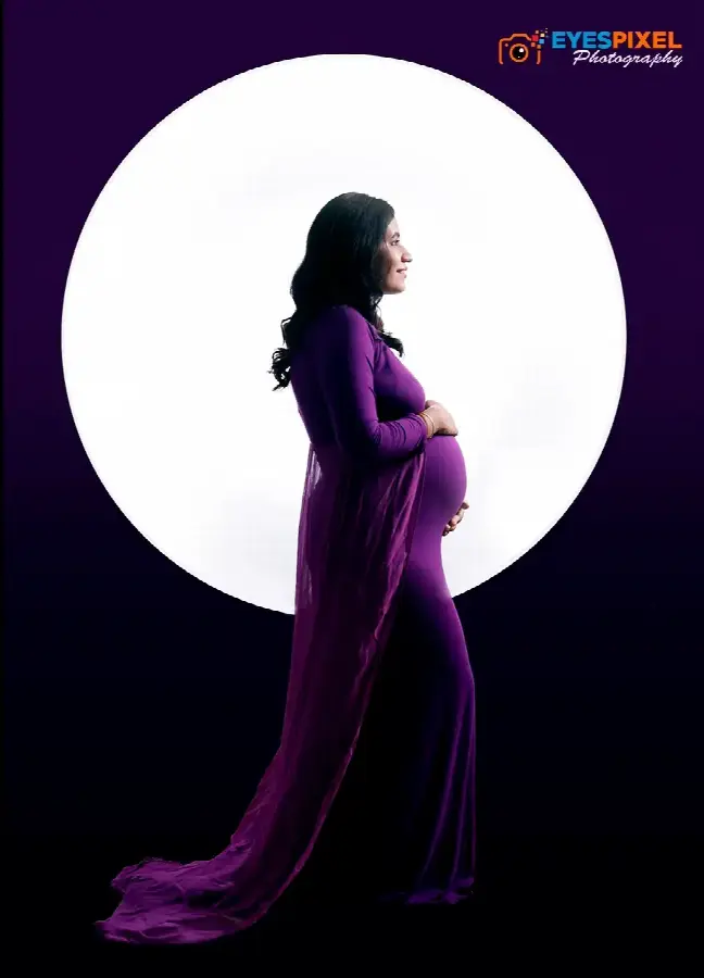 Expectant mother in a trailing purple gown lit against a large circular backdrop, Pune studio