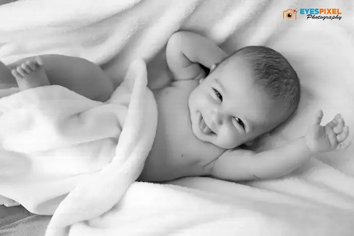 Black and white portrait of a smiling baby lying on a soft white blanket, Pune studio