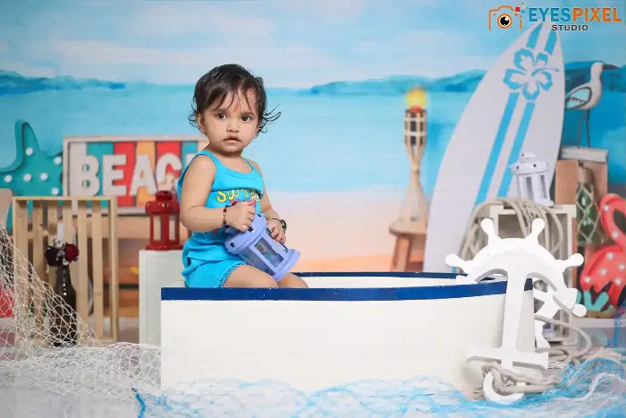 Toddler in a blue outfit sitting in a boat prop on a beach-themed studio set in Pune