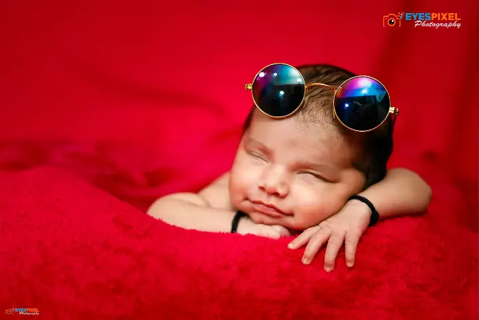 Close-up of a sleeping newborn resting on their hands, wearing round prop sunglasses, Pune studio