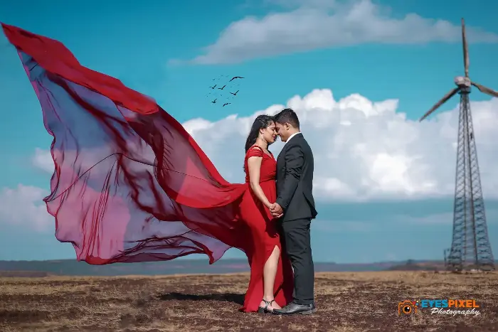 Couple forehead to forehead as a long red veil billows out behind her, wind turbine beyond