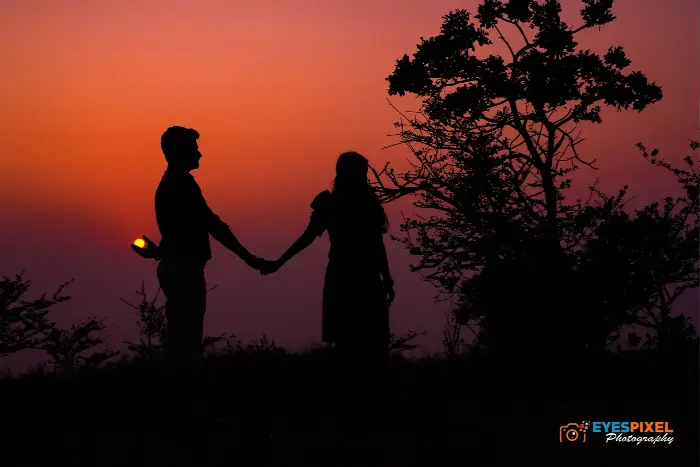 Silhouette of a couple holding hands at dusk, one holding a small light