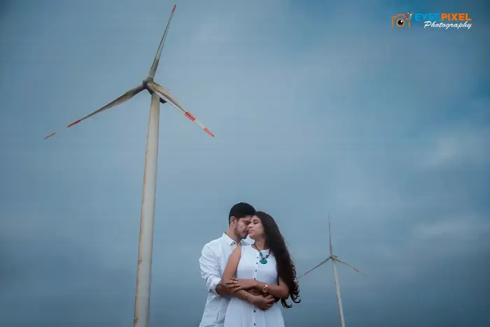 Couple in white embracing beneath wind turbines against a blue sky