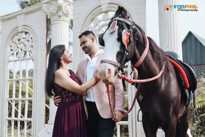 Couple beside a decorated horse at a white pillared venue, she looking up at him