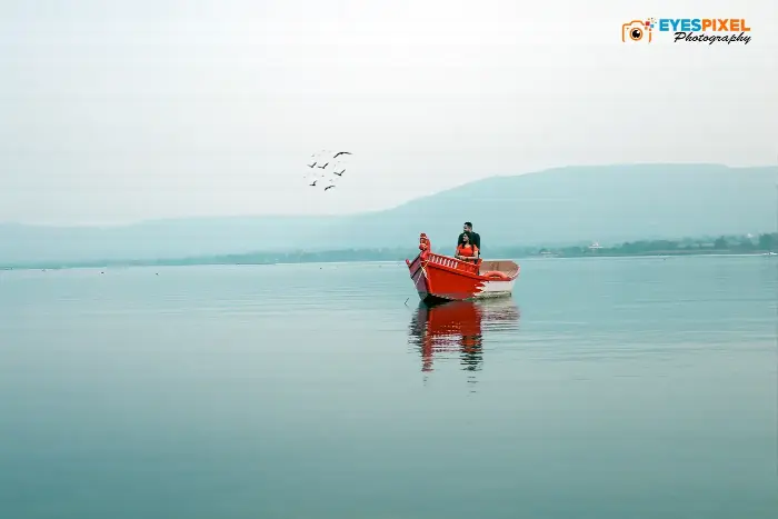 Distant view of a couple in a red boat on calm water beneath low hills