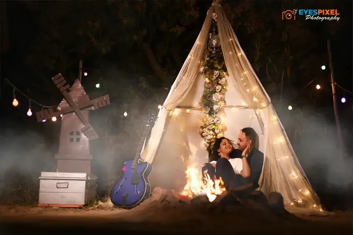Couple beside a campfire under a lit canopy strung with fairy lights at night
