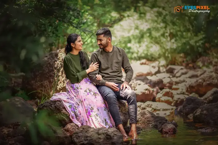 Couple sitting on rocks beside a forest stream, laughing together