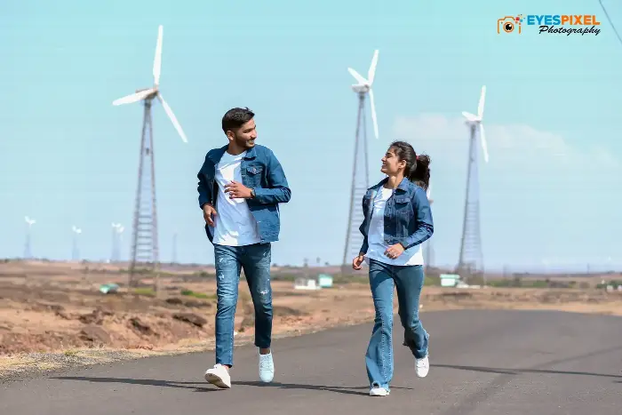Couple in denim walking a road through a wind farm, laughing at each other