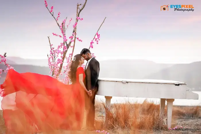 Couple beside a white piano in open country, her red gown spread across the grass