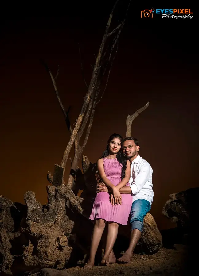 Couple lit against bare driftwood at night, warm amber sky behind them
