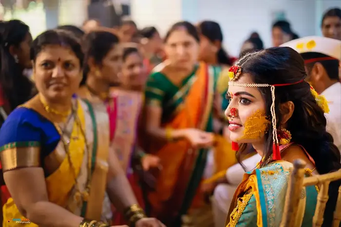 Bride with turmeric on her face seated among family during the haldi ceremony