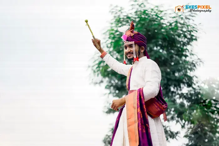 Groom in a purple pheta raising a ceremonial staff against the sky