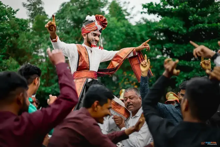 Groom dancing with arms outstretched, guests celebrating around him at the procession