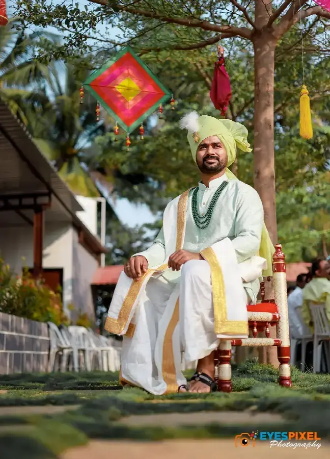 Groom in a green pheta seated outdoors beneath kite decorations before the ceremony