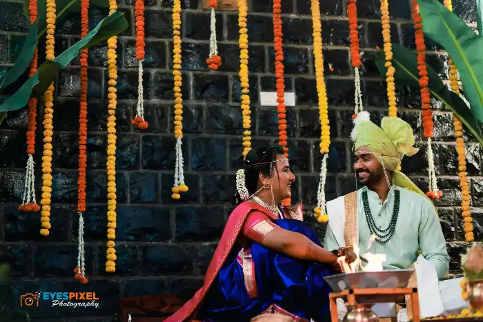 Bride and groom laughing together in front of a stone wall hung with marigold garlands