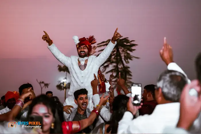 Groom lifted on shoulders with arms raised, celebrating amid the wedding procession