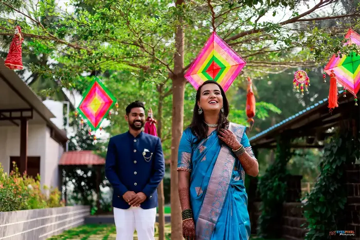 Bride in a blue silk saree laughing under kite decorations, groom watching from behind