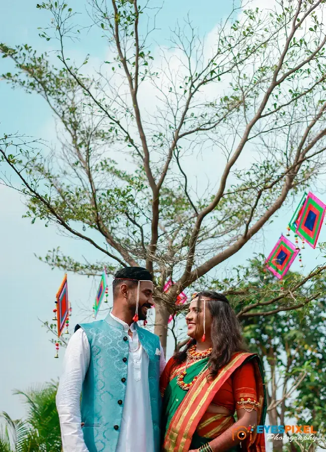 Bride and groom in traditional dress looking at each other beneath a tree with hanging decorations