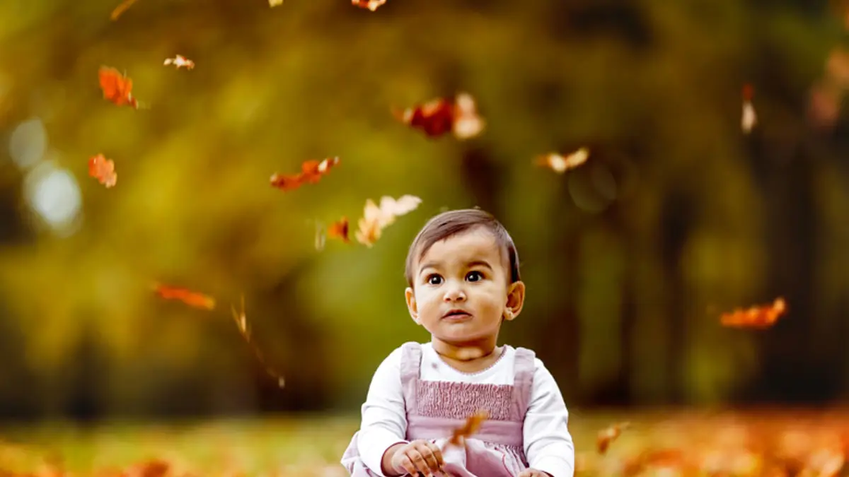 Baby sitting among falling autumn leaves in a park, photographed in Pune