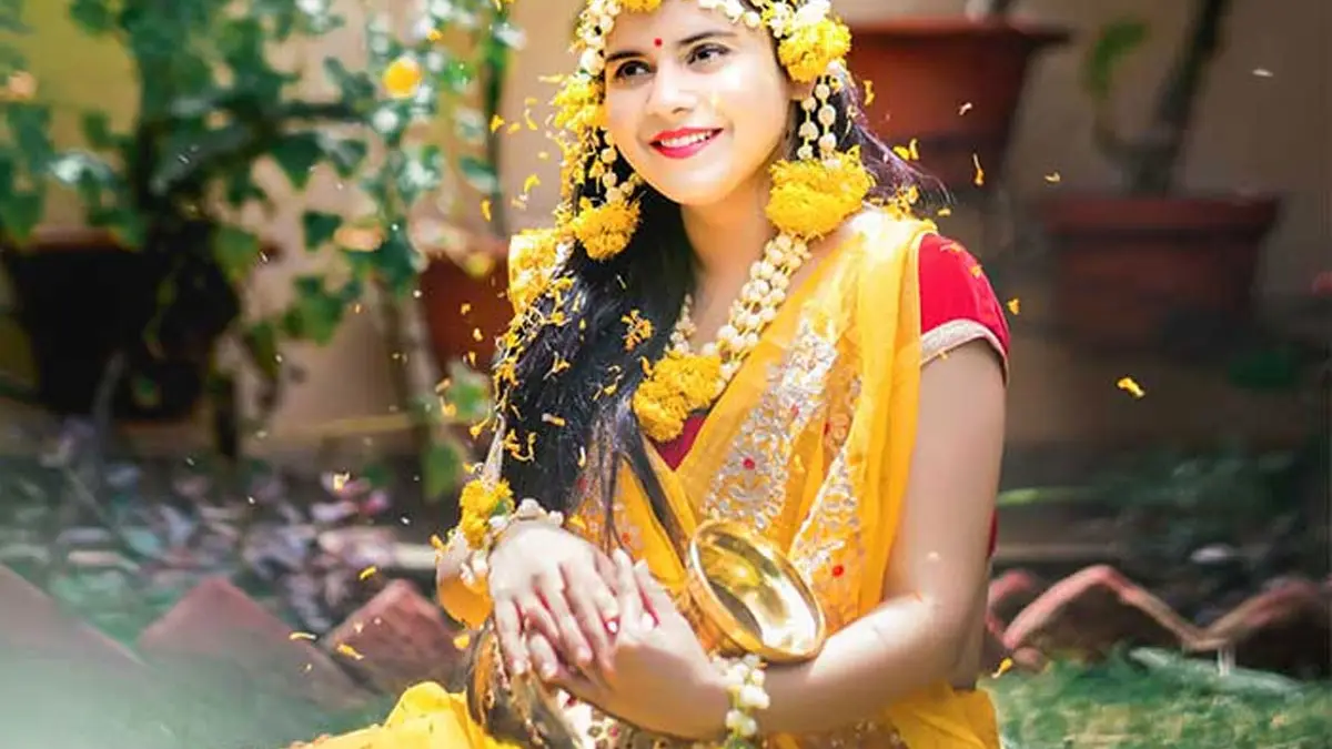Bride covered in marigold petals during her haldi ceremony, holding a brass bowl